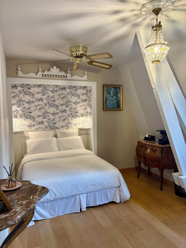 Ein Schlafzimmer mit einem Bett, einem Deckenventilator, einer Pendelleuchte, einem Nachttisch und einem Bild an der Wand.