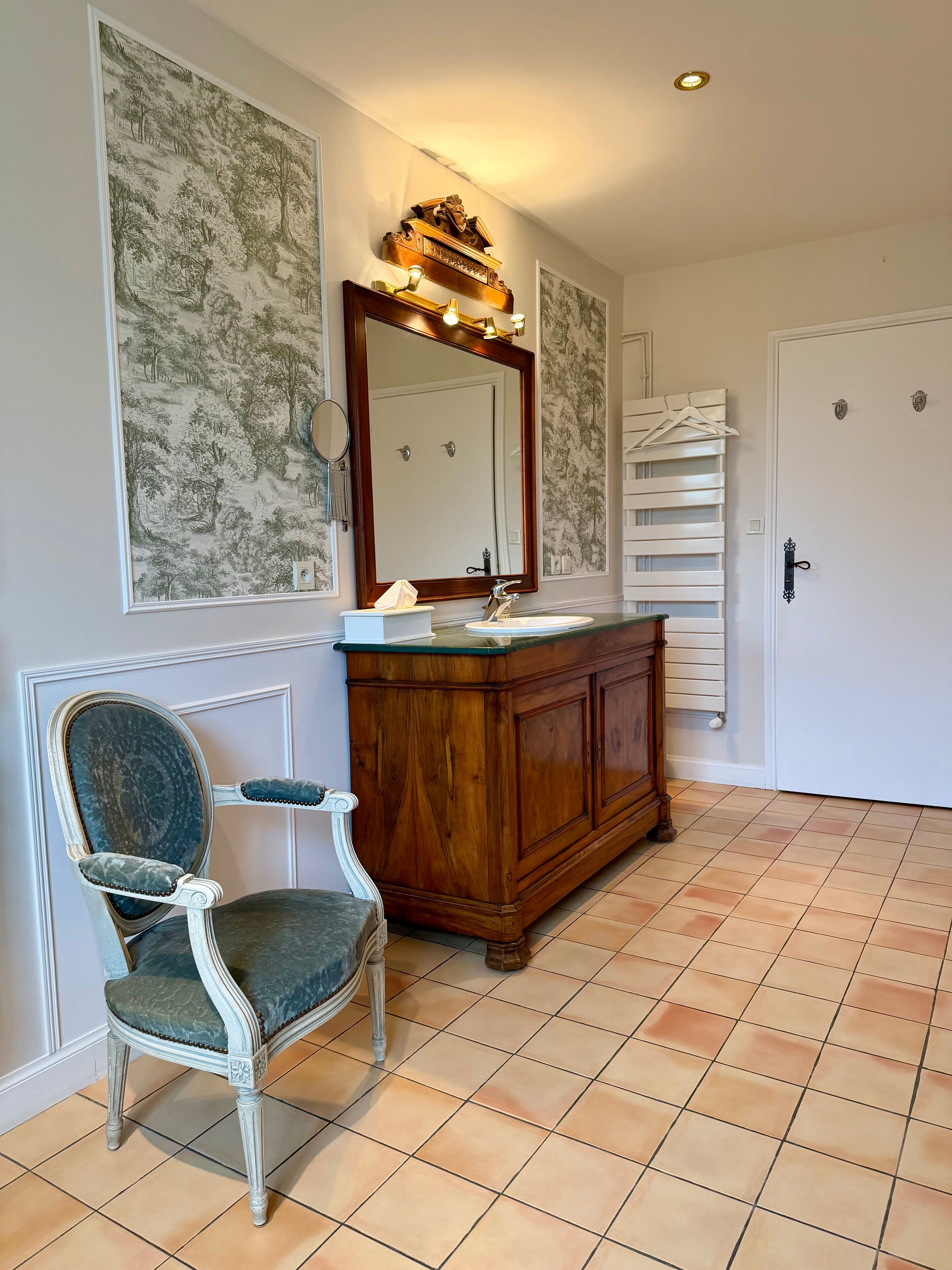 A bathroom with a wooden vanity, a large mirror, and a vintage chair.