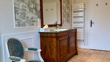 A bathroom with a wooden vanity, a large mirror, and a vintage chair.
