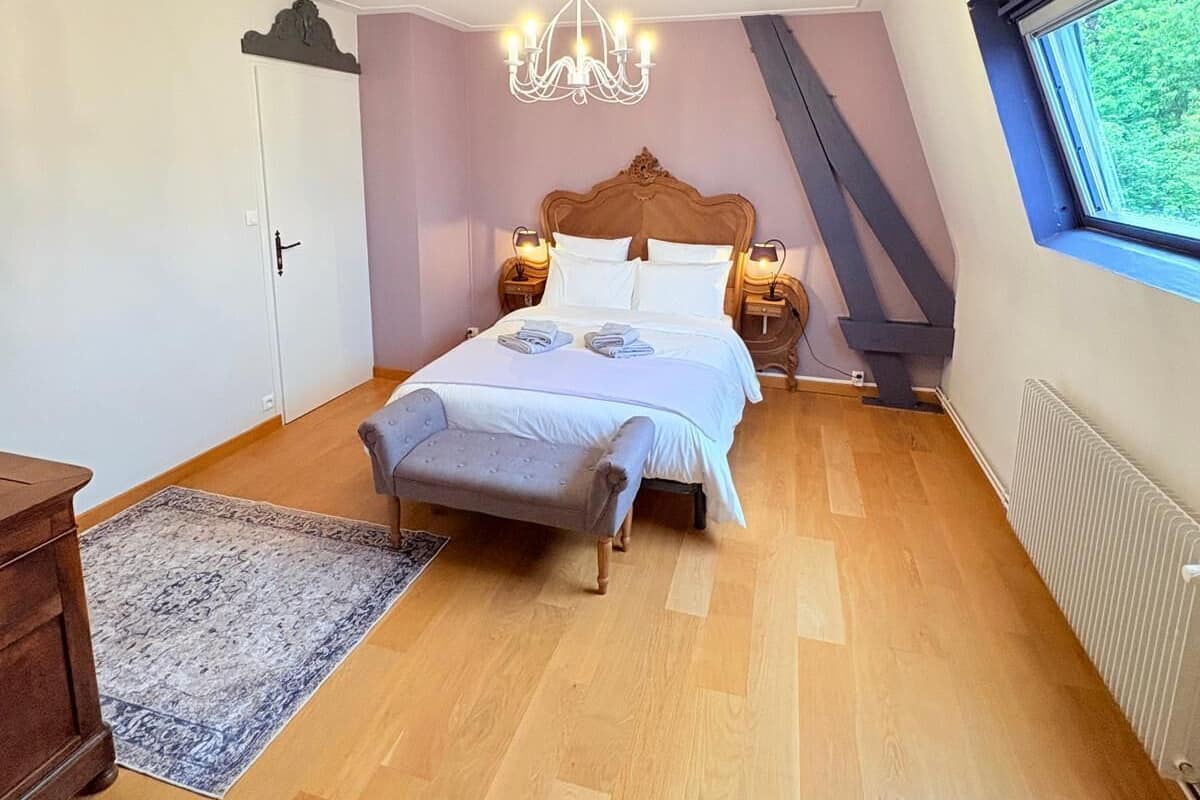 Een slaapkamer met een houten bed, een kroonluchter, een nachtkastje, een raam met uitzicht en een radiator.