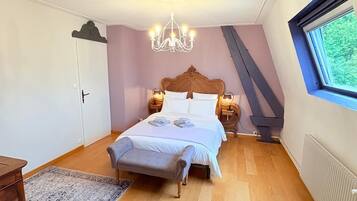 A bedroom with a wooden bed, a chandelier, a nightstand, a window with a view, and a radiator.