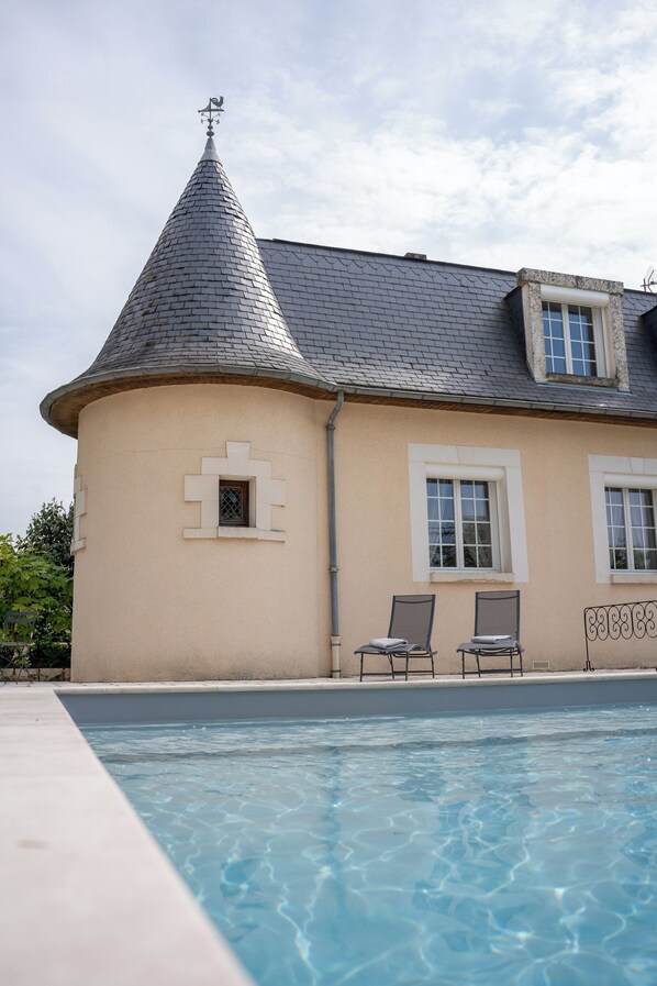 Un edificio con techo cónico, piscina y dos sillones de descanso.