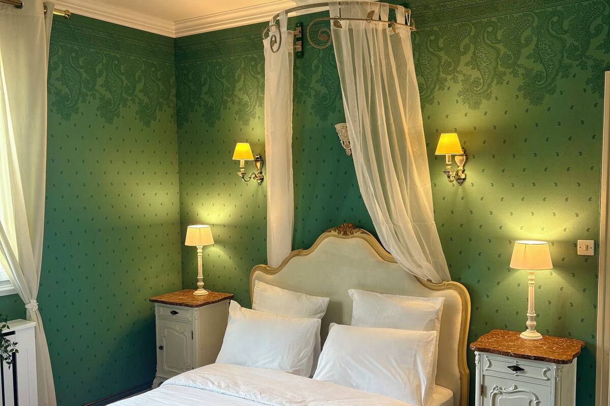 Een slaapkamer met een hemelbed, twee nachtkastjes met lampen, en behang met een groen patroon.