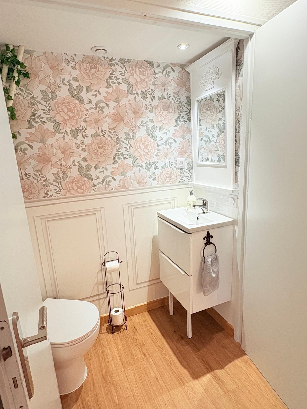 Une salle de bain avec un papier peint à motifs floraux, un lavabo blanc et des toilettes.