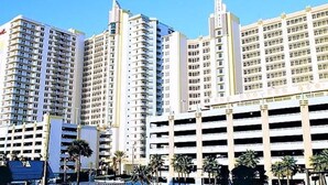 A high-rise hotel with multiple floors, a parking garage, and palm trees in the foreground.