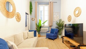 Ein Wohnzimmer mit einem beigen Sofa, einem blauen Sessel, einem Fernseher und dekorativer Wandweberei.