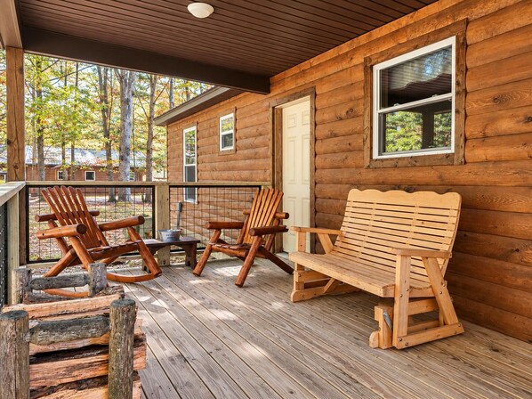 A wooden cabin with a porch, two rocking chairs, and a bench.