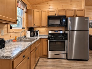 A kitchen with wooden cabinets, a stainless steel refrigerator, a microwave, a stove, and a sink.