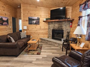 A cozy living room with a fireplace, wooden walls, a flat-screen TV, and leather furniture.