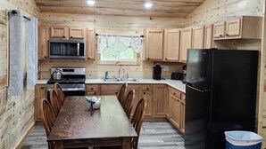 A kitchen with wooden cabinets, a dining table with chairs, a black refrigerator, and a microwave.
