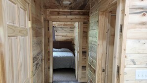 A narrow hallway with wooden walls and a carpeted floor leading to a bedroom with a bed.