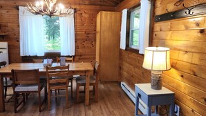 A wooden cabin interior with a dining table, chairs, a chandelier, and a window with curtains. - Secluded Red Maple Cabin (Vowinckel)