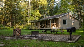 A cabin with a porch, picnic tables, a grill, and a fire pit in a wooded area. - Secluded Red Maple Cabin (Vowinckel)