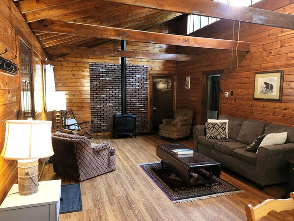 A cozy cabin interior with a fireplace, wooden walls, a sofa, and a patterned rug.
