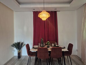 Ruokailutila, jossa on neljälle katettu ruokapöytä, kattokruunu ja punainen verho.