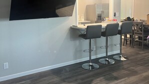Una cocina moderna con un televisor de pantalla plana grande montado en la pared, una zona de bar con tres taburetes y una mesa de comedor con sillas.