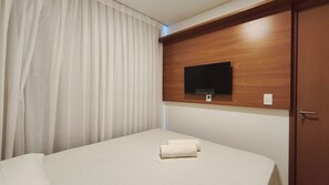 A hotel room with a bed, a TV mounted on a wooden panel, a door, and a curtain.