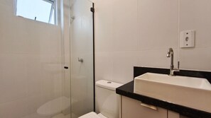 Casa de banho com chuveiro em cabine de vidro, sanita branca e lavatório com bancada preta.