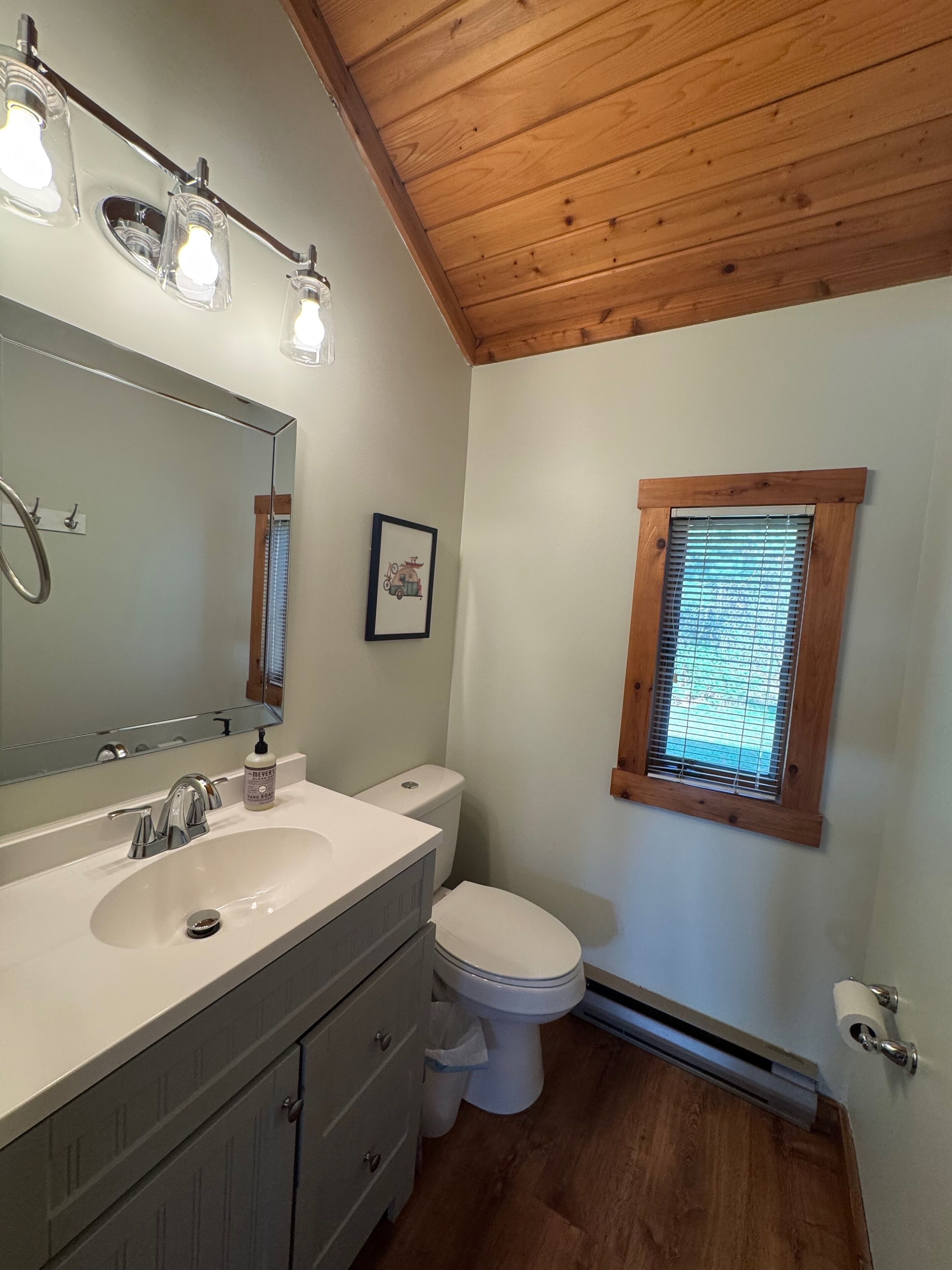 A bathroom with a white sink, a mirror, a toilet, and a window with blinds.