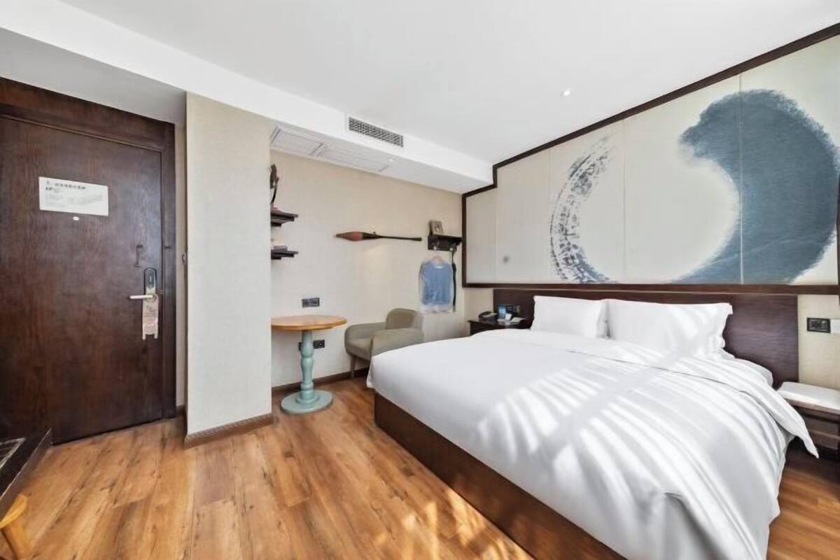Habitació d'hotel amb un llit gran, un terra de fusta, escriptori, cadira i una paret amb un quadre abstracte de grans dimensions.