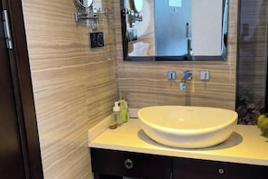 Un baño moderno con un lavabo grande y redondo, un espejo y un mueble de tocador con un gabinete oscuro.