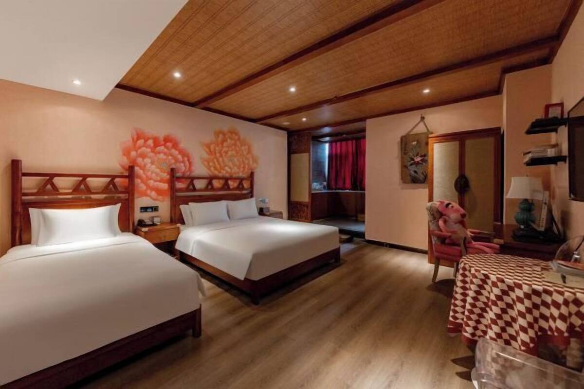 Habitació d'hotel amb dos llits, sostre de fusta, un mural floral gran a la paret, cortina vermella i un mantell de taula amb quadres.