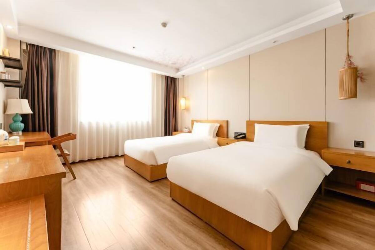 Habitació d'hotel amb dos llits, un escriptori de fusta, una làmpada i vista cap a l'exterior.
