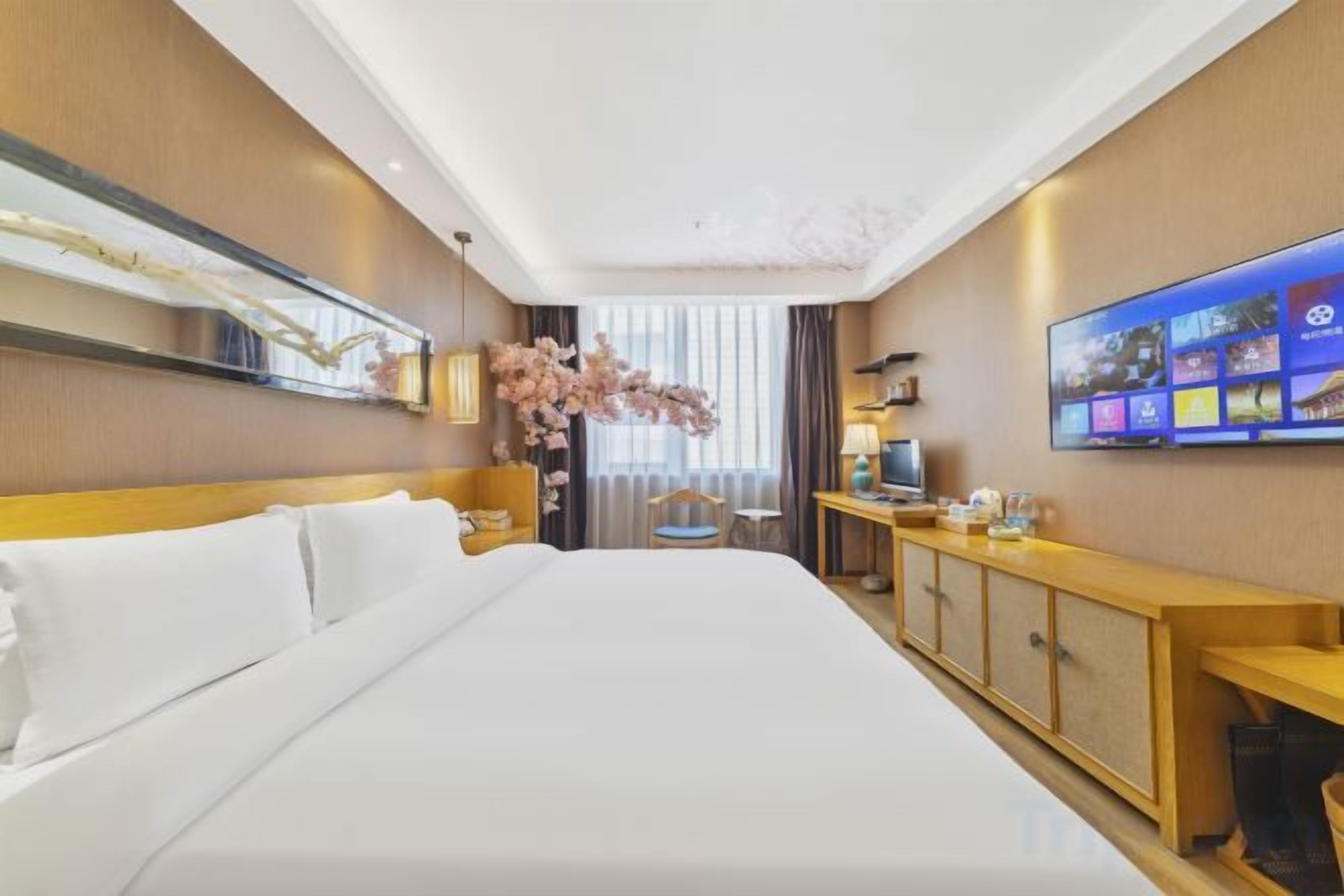 A hotel room with a large bed, a desk with a chair, a television, and a window with curtains.
