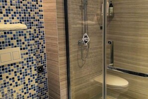 Un baño con pared de azulejos, cabina de ducha de vidrio y un inodoro.