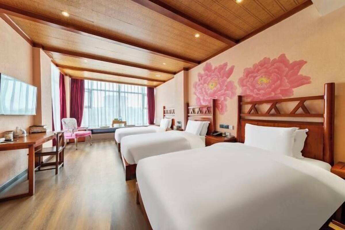 Habitació d'hotel amb quatre llits, bigues de sostre de fusta, una finestra gran amb cortines i una paret amb un mural floral gran.