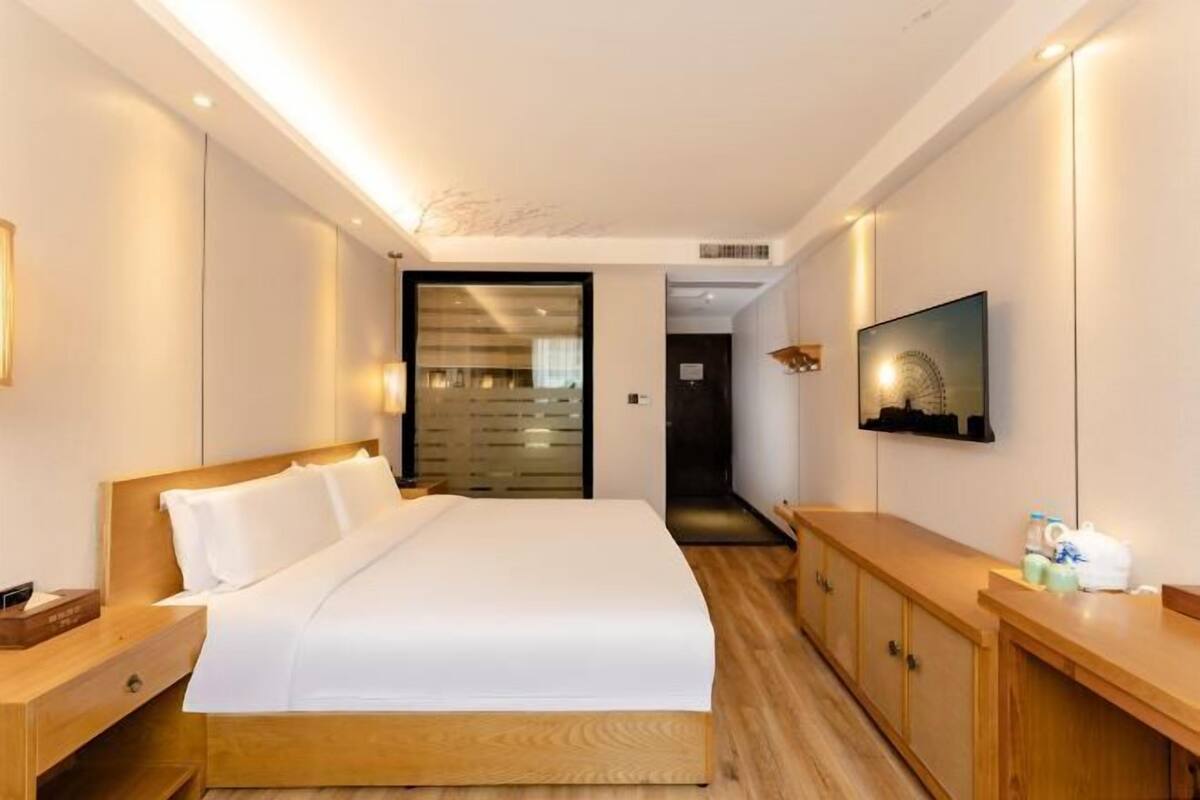 Habitació d'hotel amb un llit gran, un panell de capçal de fusta, taules de nit, televisió i un armari.