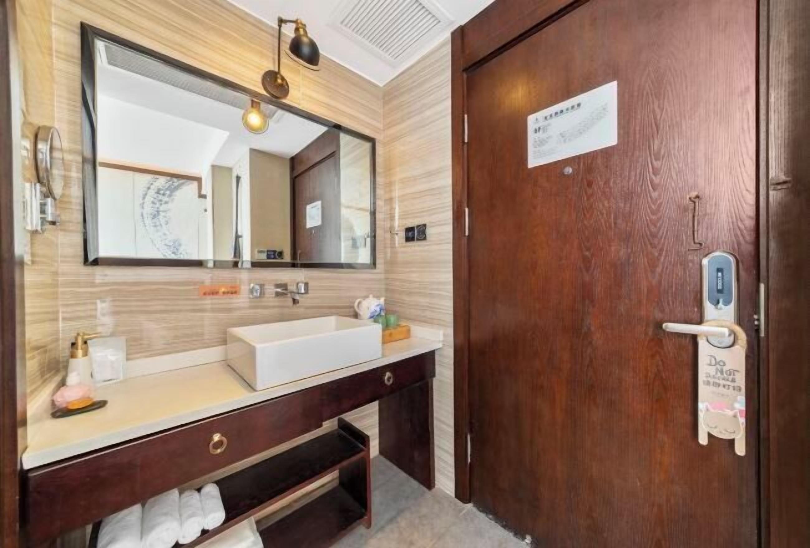 A hotel bathroom with a wooden vanity, a large mirror, a sink, and a towel rack.
