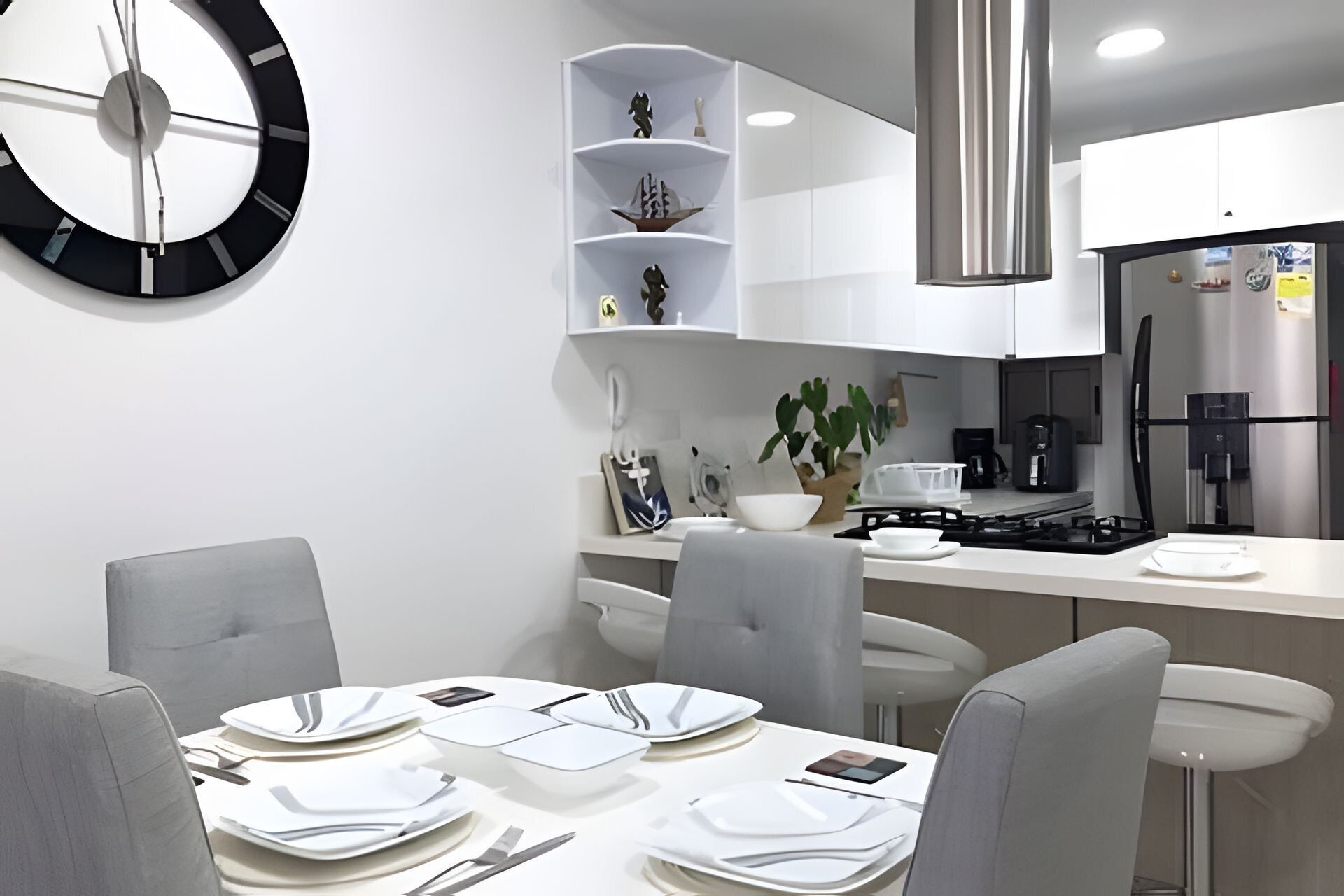 Cozinha moderna com armários brancos, coifa de aço inoxidável e área de jantar com mesa redonda para quatro pessoas.