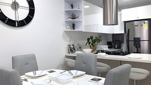 Una cocina moderna con gabinetes blancos, una campana extractora de acero inoxidable y un comedor con una mesa redonda para cuatro comensales.