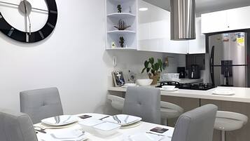Cozinha moderna com armários brancos, coifa de aço inoxidável e área de jantar com mesa redonda para quatro pessoas.