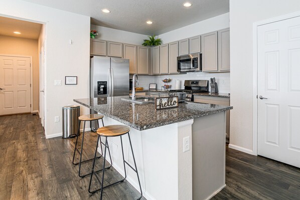 A modern kitchen with a central island, bar stools, stainless steel appliances, and a microwave.