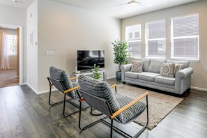 A modern living room with a grey sofa, two armchairs, a flat-screen TV, and a potted plant.