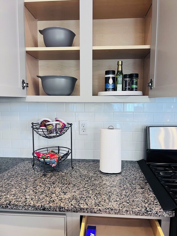Une cuisine dotée de plans de travail en granit, d’une cuisinière à gaz, d’un porte-rouleau à essuie-tout et d’un étagère à épices.