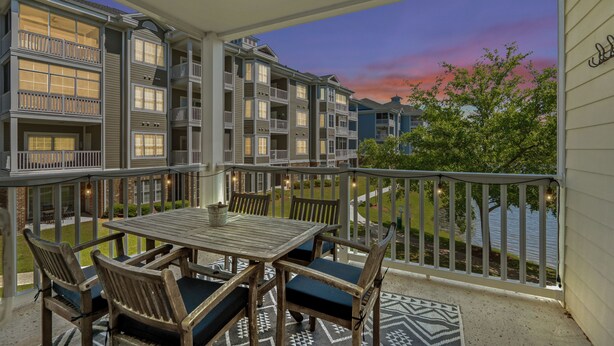 A balcony with a table and chairs, overlooking a residential area with a sunset view. - Bright and Modern 3BR Family Friendly Condo with pool, golf, Ripken Experience. (Myrtle Beach)