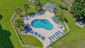 An aerial view of a swimming pool area with sun loungers, palm trees, and a small building. - Bright and Modern 3BR Family Friendly Condo with pool, golf, Ripken Experience. (Myrtle Beach)