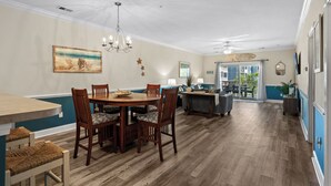 A spacious dining area with a wooden table and chairs, a chandelier, and a painting on the wall. - Bright and Modern 3BR Family Friendly Condo with pool, golf, Ripken Experience. (Myrtle Beach)