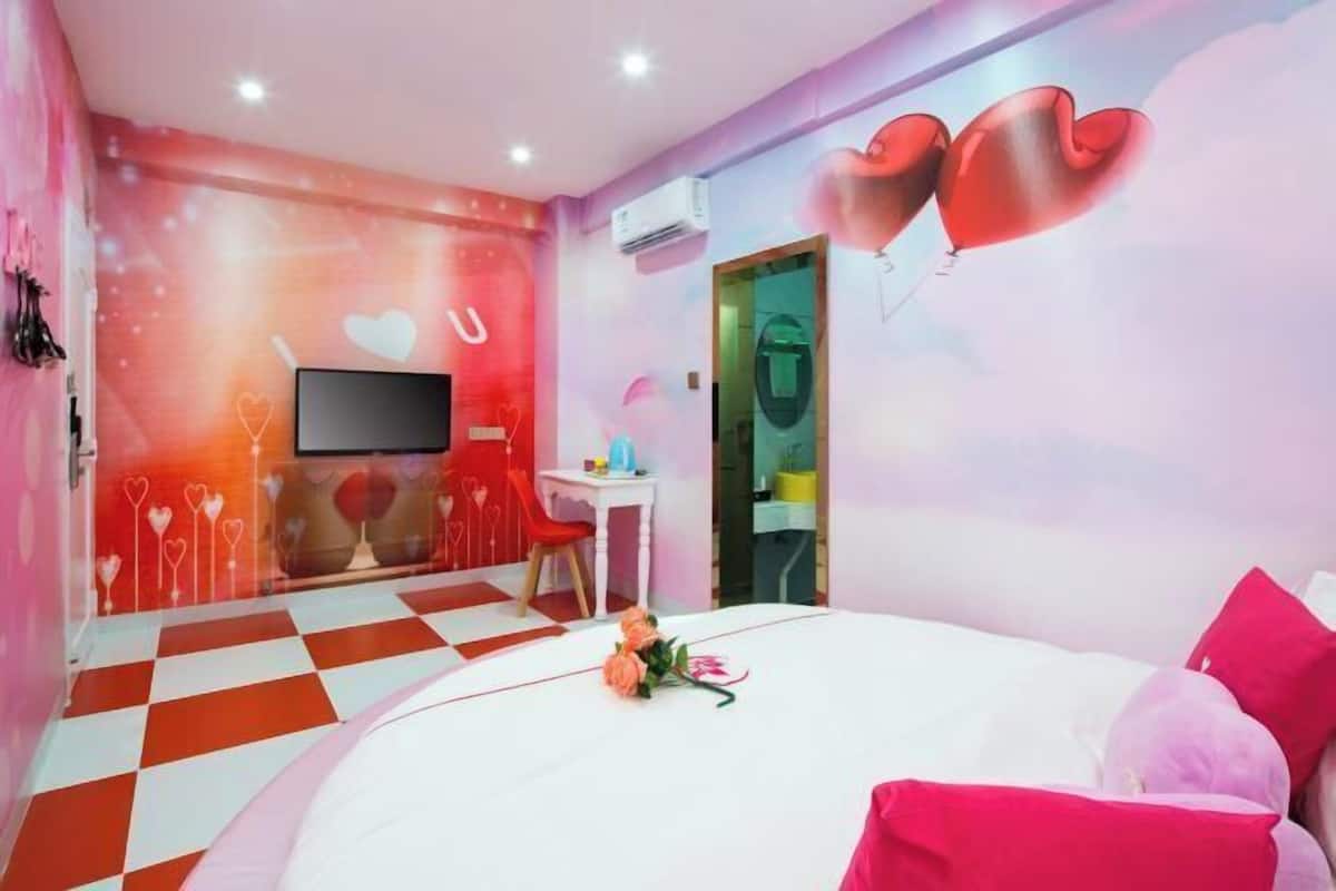 A room with a checkered floor, a bed with pink and white bedding, a TV, and a wall with heart-shaped decorations.