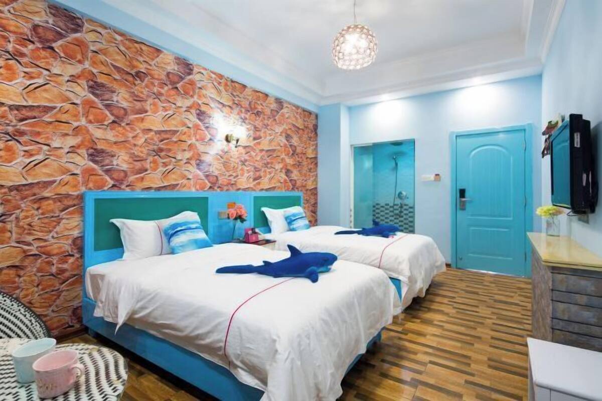 A room with two beds, a stone wall, a blue door, and a television on the wall.