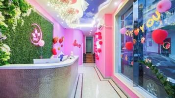 A reception area with a reception desk, a green wall with foliage, and a window with red decorations.