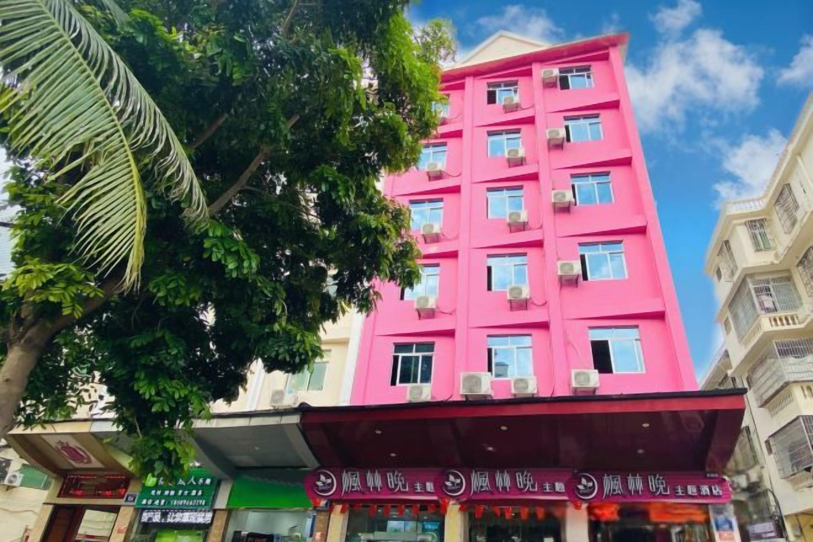 A multi-story building with a prominent pink facade, several windows, and a visible entrance with signage.