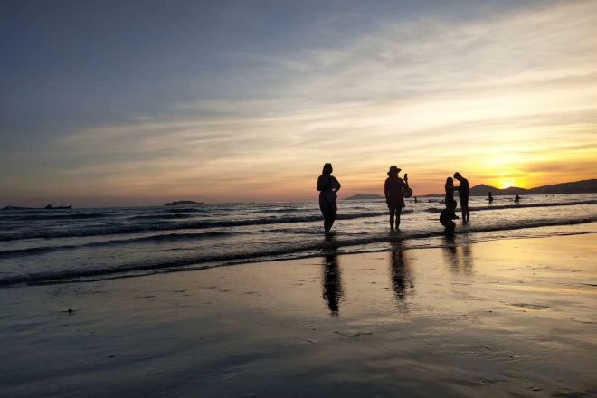 Escena de playa con gente caminando por la orilla al atardecer.