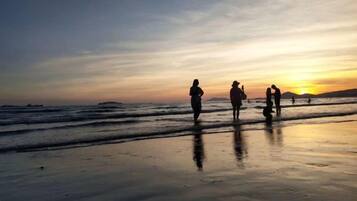 Escena de playa con gente caminando por la orilla al atardecer.