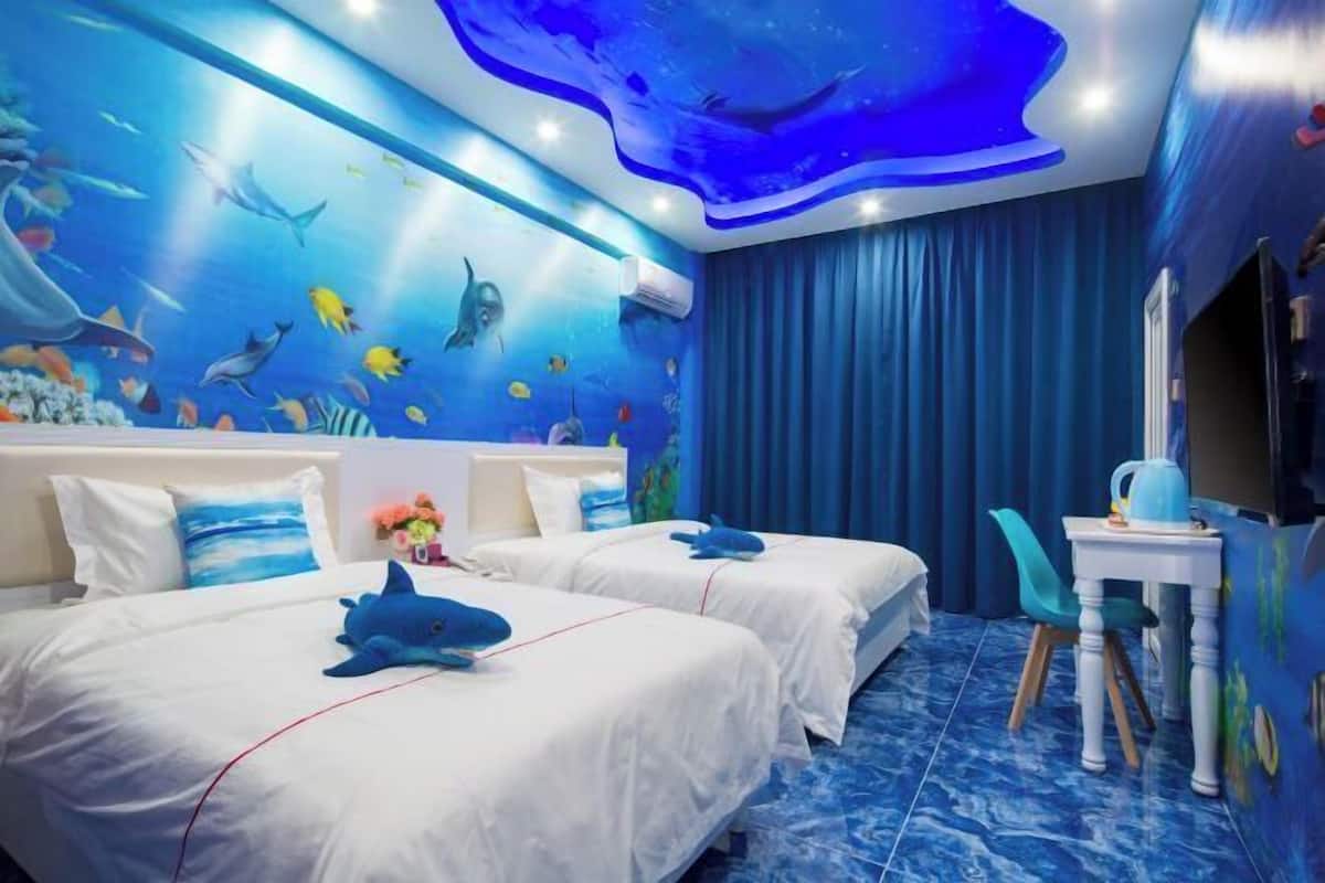 A room with two beds, a desk, and a mural of an underwater scene.