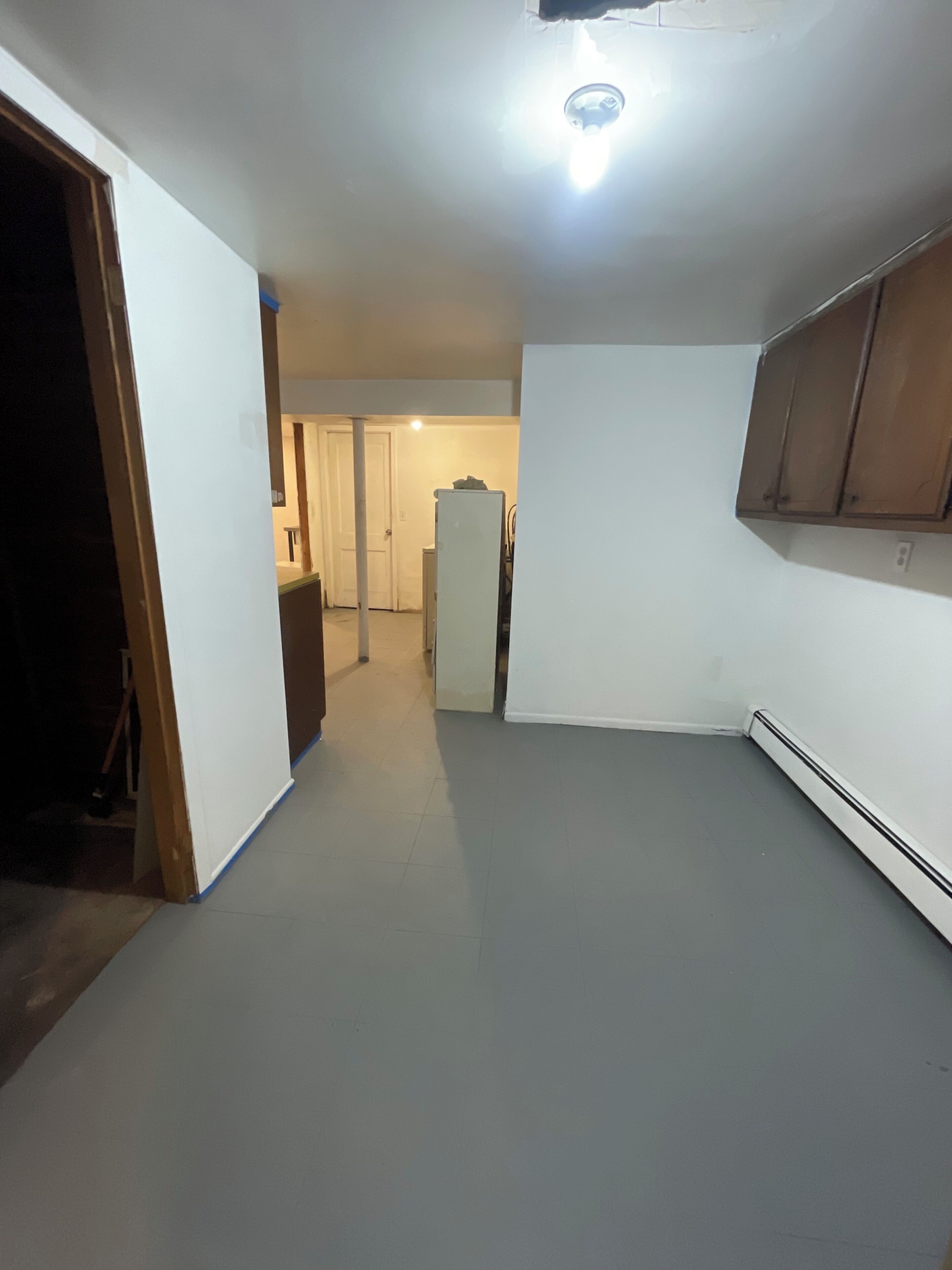Un couloir étroit, avec une porte blanche au fond, un réfrigérateur blanc et un meuble en bois.