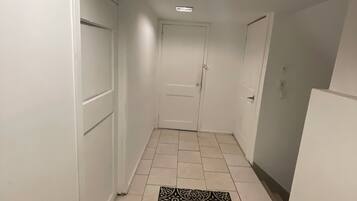 A narrow hallway with white walls, a patterned rug, and a ceiling light.